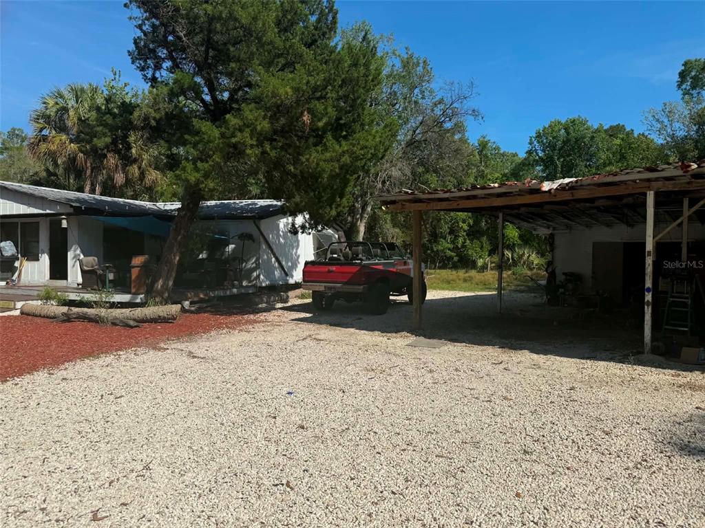 A gravel driveway leads to a mobile home and a detached open-sided carport — 186 GLADYS AVENUE, INGLIS, FL