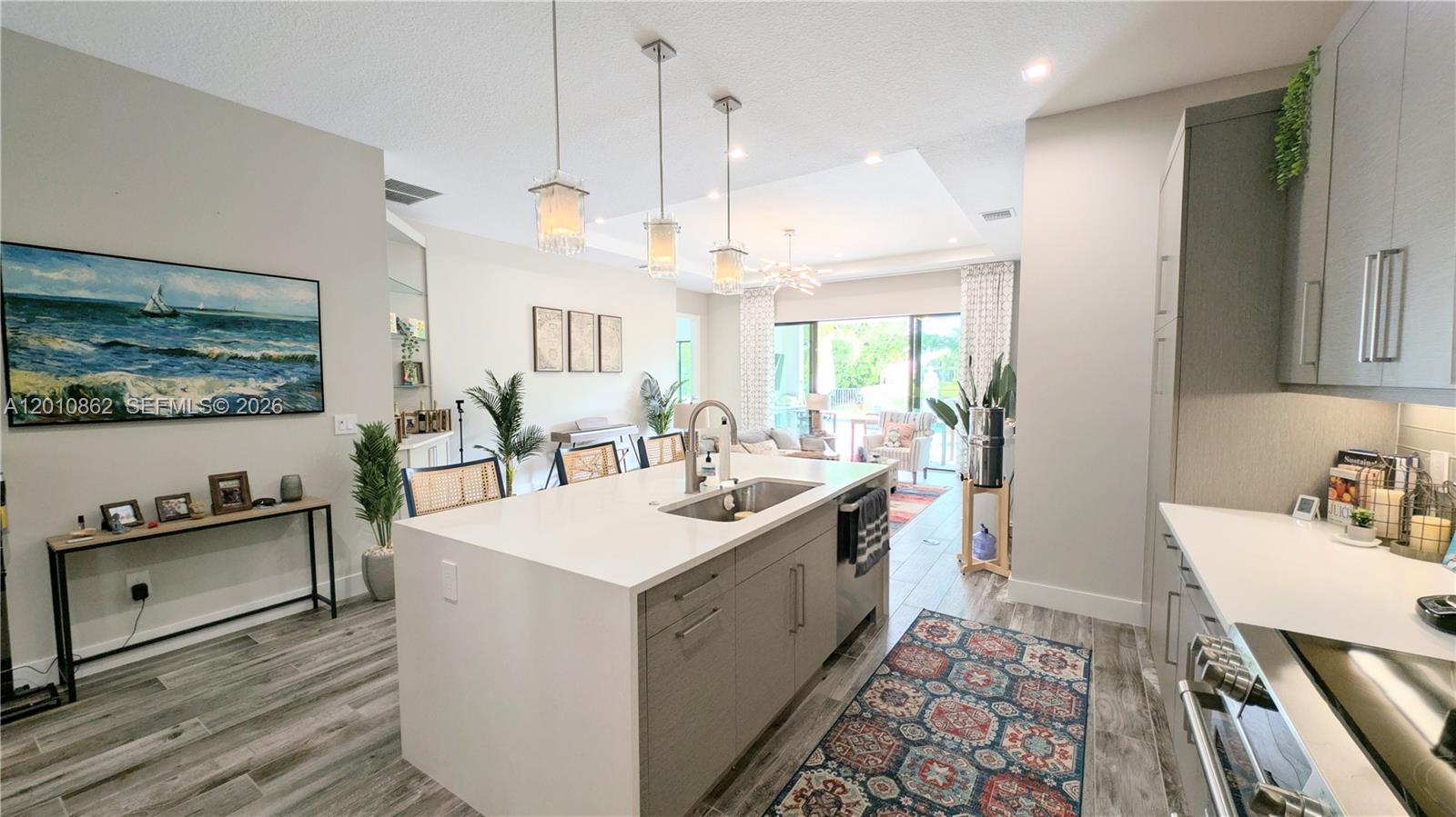 A modern kitchen features a large white island, gray cabinetry, and an open living area — 2879 Gin Berry Way, West Palm Beach FL 33401, WEST PALM BEACH, FL