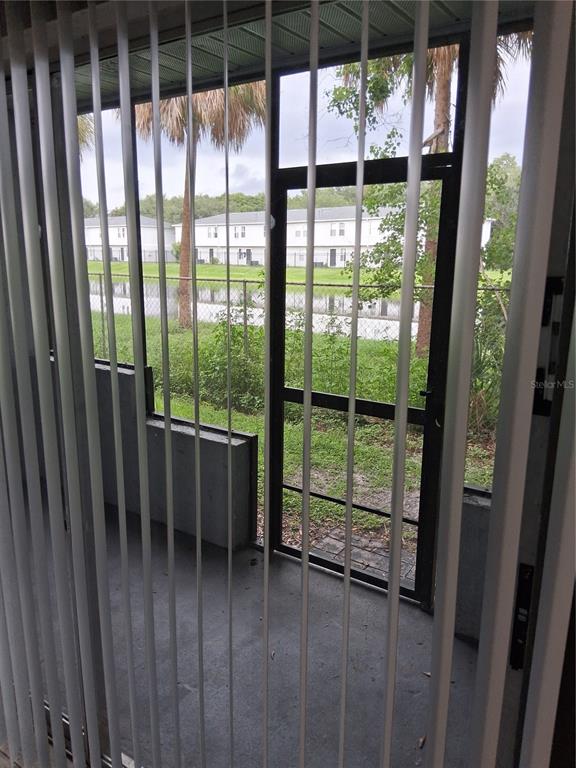 A view from inside through vertical blinds to a screened porch overlooking a grassy area — 4733 S TEXAS AVENUE UNIT 4733B, ORLANDO, FL