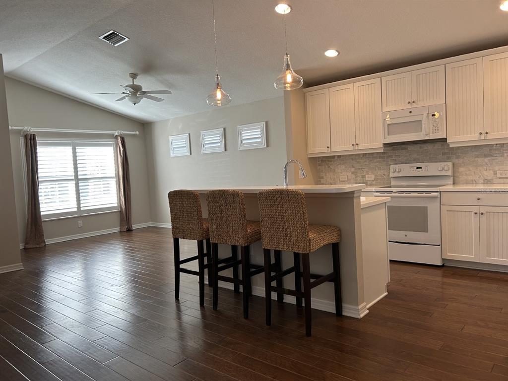 A kitchen with white cabinets, a breakfast bar with three stools, and dark wood flooring — 12721 SAGEWOOD DRIVE, VENICE, FL