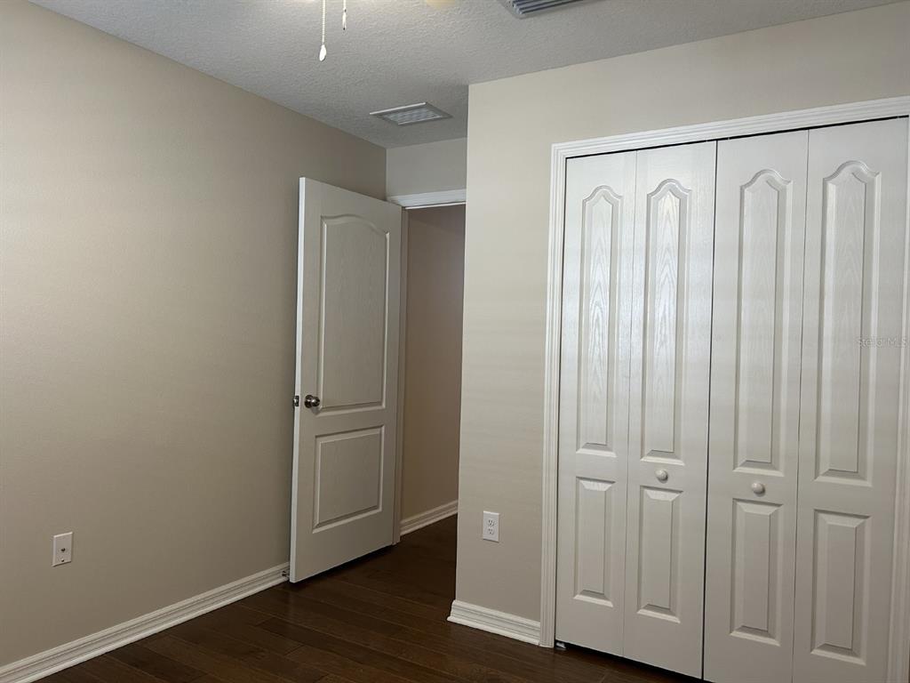 A bedroom with beige walls, dark wood flooring, a white door, and white closet doors — 12721 SAGEWOOD DRIVE, VENICE, FL