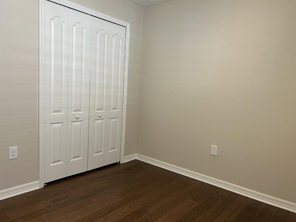 A bedroom with dark wood-look flooring, beige walls, and white bi-fold closet doors — 12721 SAGEWOOD DRIVE, VENICE, FL