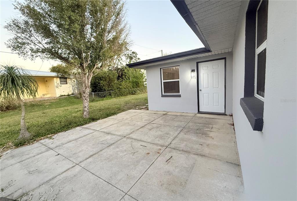 A concrete patio sits outside a gray house with a white door and two windows — 134 PEACE ISLAND DRIVE, PUNTA GORDA, FL