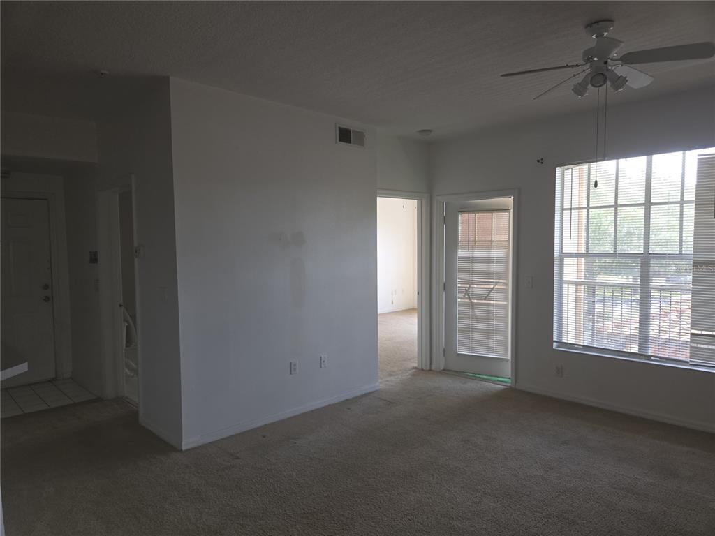 An interior view of a carpeted living room with a ceiling fan and sliding glass door — 5566 METROWEST BOULEVARD UNIT 2-205, ORLANDO, FL