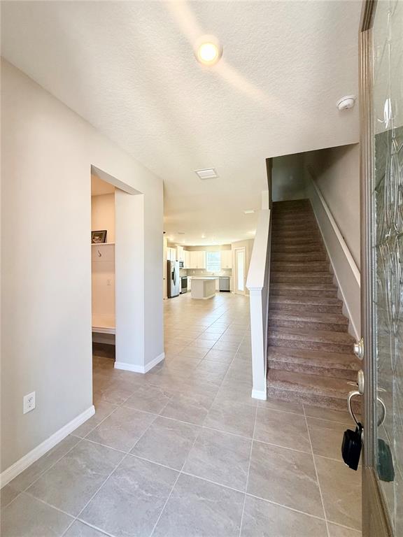 An entryway with tile flooring leads to a staircase and an open-concept kitchen beyond — 30877 QUAIL CAPER CIRCLE, SAN ANTONIO, FL