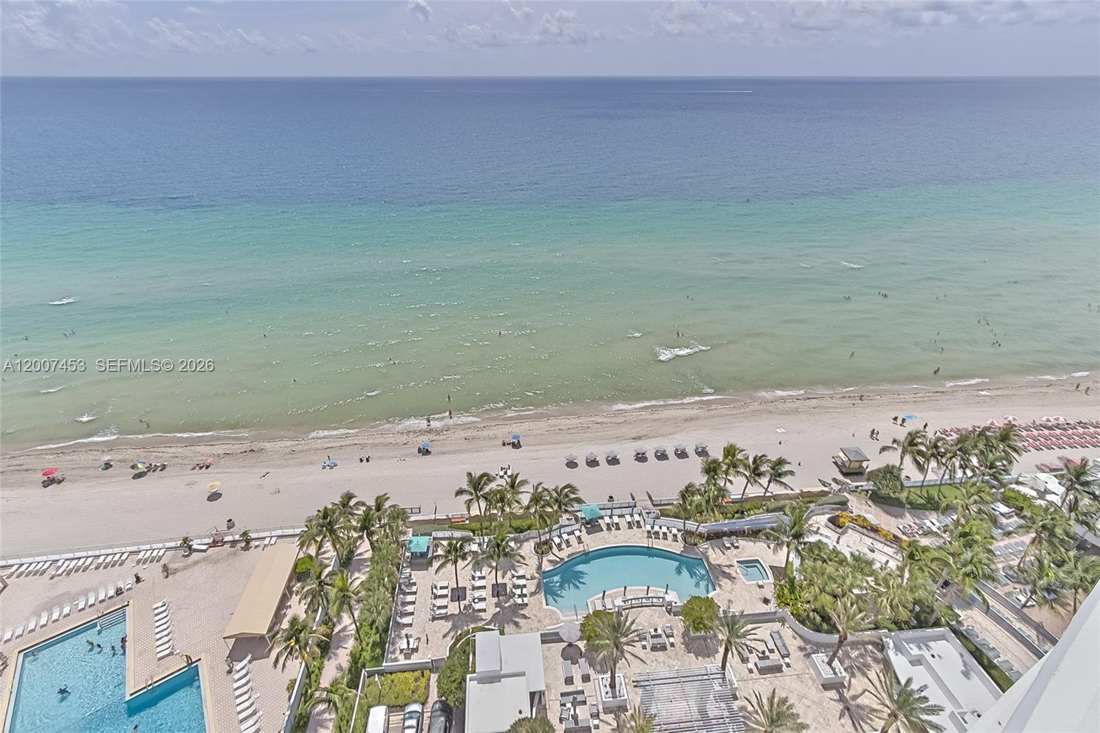 An aerial view shows a beach, ocean, and a resort pool deck with palm trees — 3535 S OCEAN DR # 2002, Hollywood FL 33019, HOLLYWOOD, FL