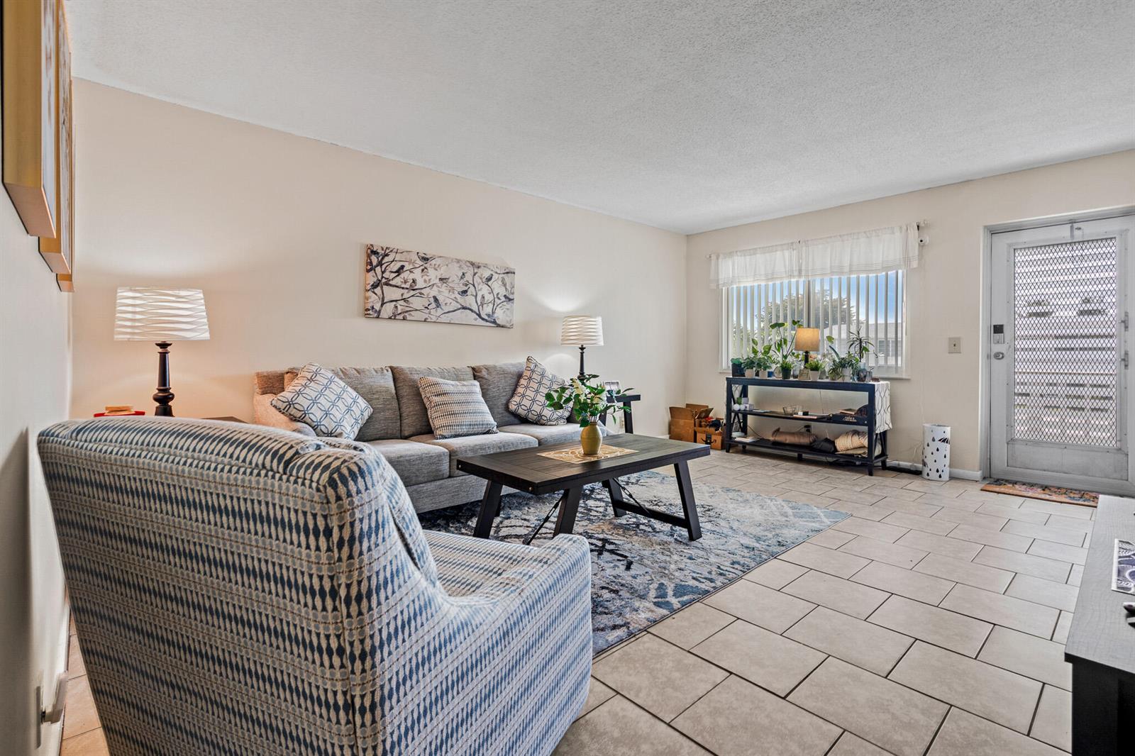 A living room features a gray sofa, patterned armchair, coffee table, and tile flooring — 167 Cambridge G, West Palm Beach FL 33417, WEST PALM BEACH, FL