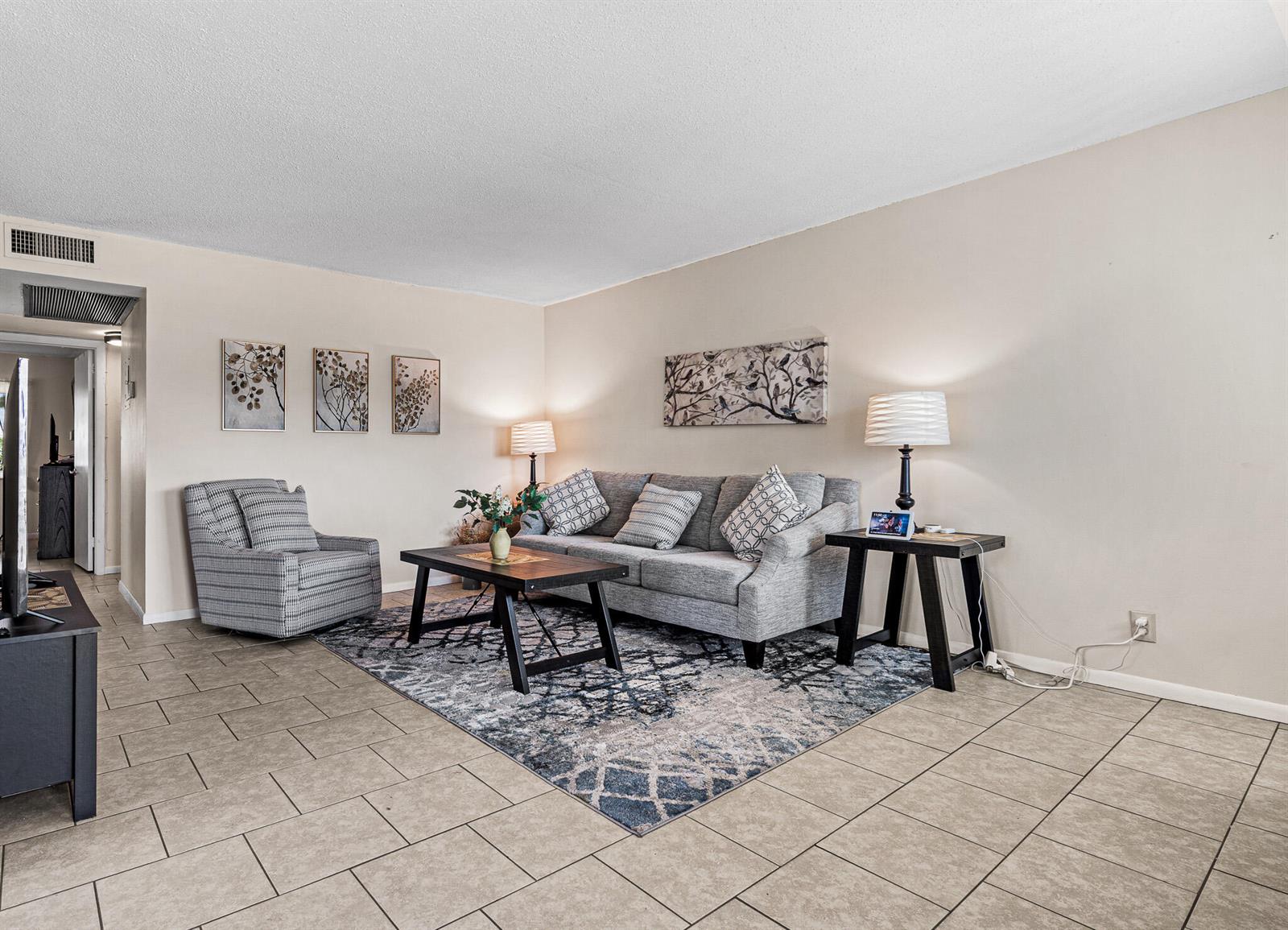 A living room features a grey sofa, a patterned area rug, and tile flooring — 167 Cambridge G, West Palm Beach FL 33417, WEST PALM BEACH, FL