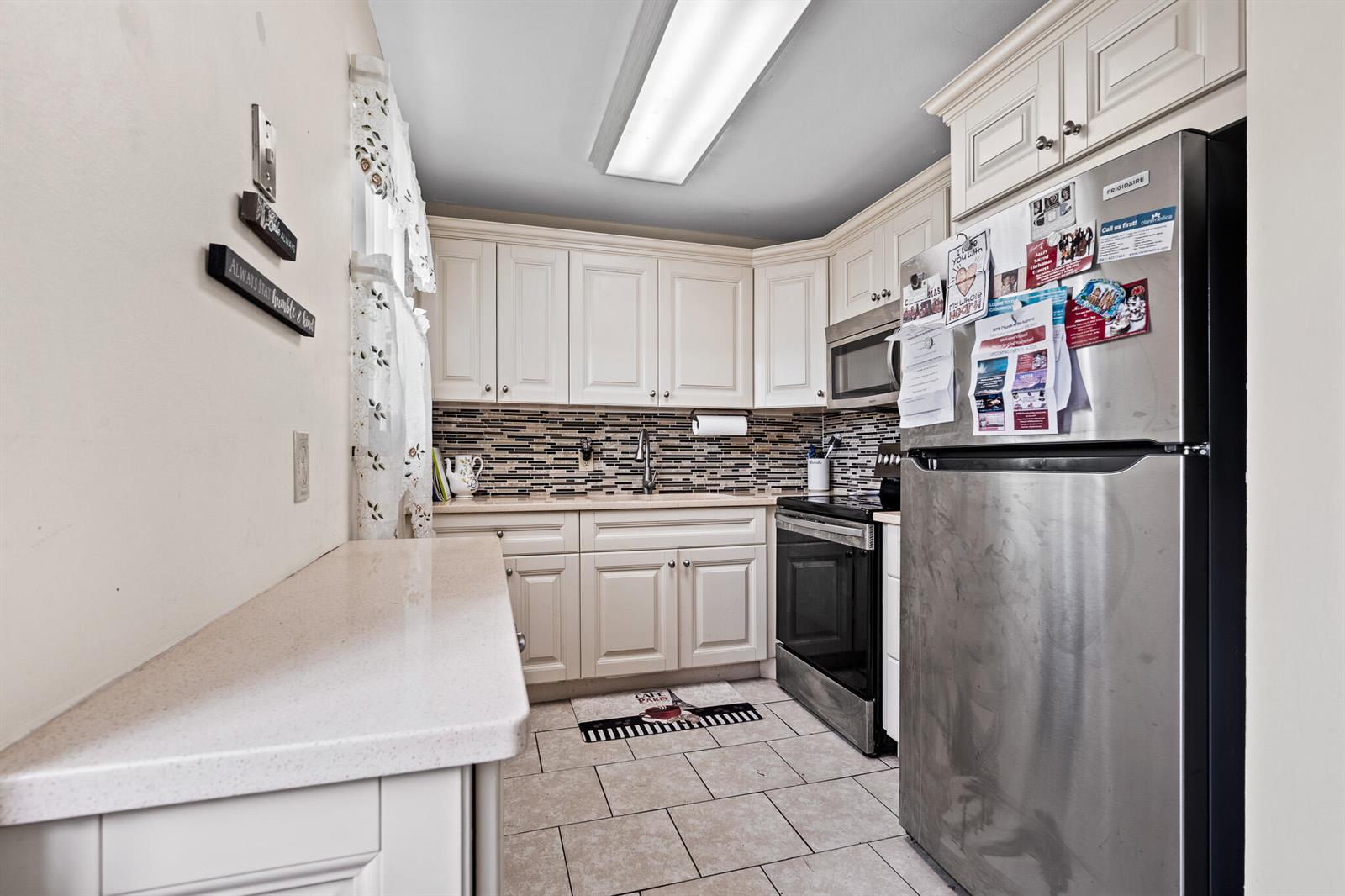 A kitchen features cream-colored cabinets, stainless steel appliances, a tiled backsplash, and light-colored countertops — 167 Cambridge G, West Palm Beach FL 33417, WEST PALM BEACH, FL