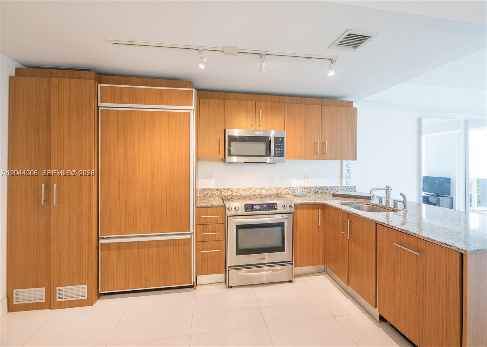 A kitchen features wood-grain cabinetry, stainless steel appliances, granite countertops, and white tile flooring — 10275 E Collins Ave # 502, Bal Harbour FL 33154, BAL HARBOUR, FL