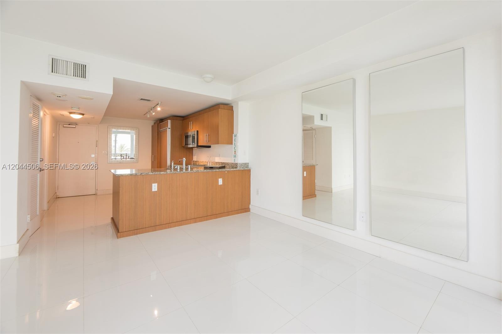 A kitchen with wood cabinets and a granite island opens into a white-tiled living area — 10275 E Collins Ave # 502, Bal Harbour FL 33154, BAL HARBOUR, FL