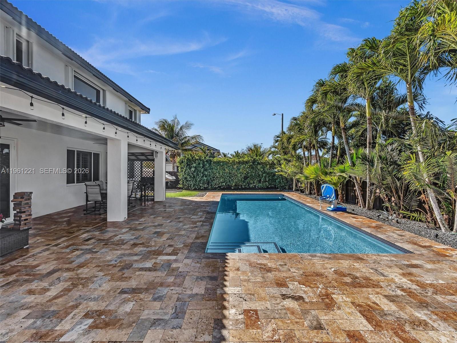 A rectangular swimming pool sits on a stone patio next to a white house — 22690 SW 127th Ct, Miami FL 33170, MIAMI, FL