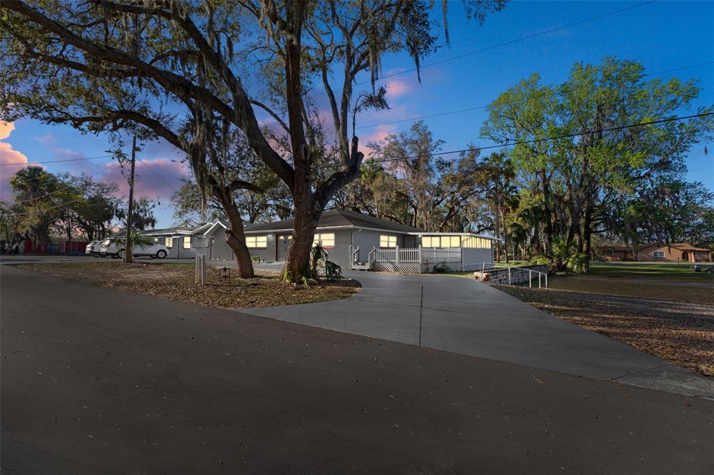 A single-story house with a concrete driveway sits under large trees at dusk — 639 NE 1ST STREET, CRYSTAL RIVER, FL
