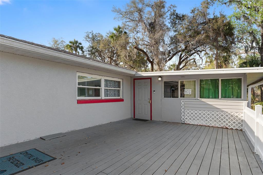 A gray wooden deck leads to a house entrance with a red-trimmed door and windows — 639 NE 1ST STREET, CRYSTAL RIVER, FL