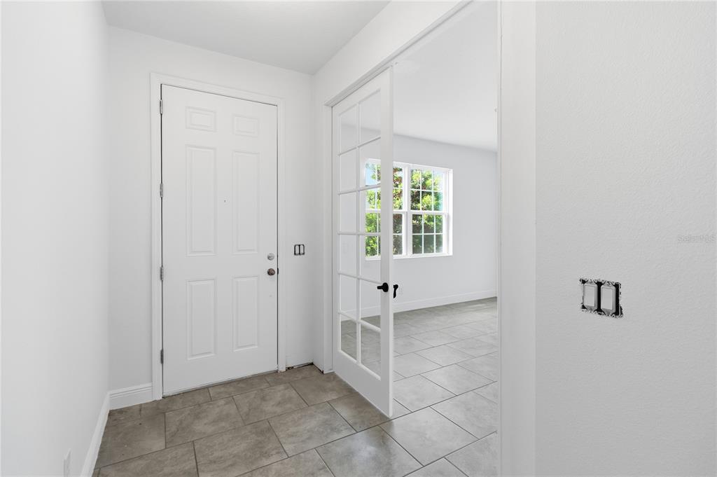 An entryway with tiled flooring, a white front door, and French doors leading to a room — 2976 NOTTEL DRIVE, ST CLOUD, FL