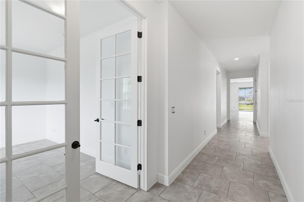 A hallway with light gray tile flooring leads to a room with French doors — 2976 NOTTEL DRIVE, ST CLOUD, FL