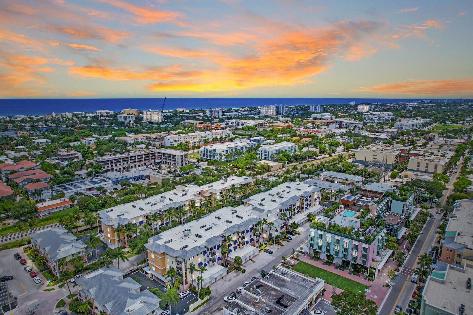 An aerial view shows a multi-story apartment complex surrounded by urban development and lush greenery — 255 NE 3rd Avenue Unit 407, Delray Beach FL 33444, DELRAY BEACH, FL