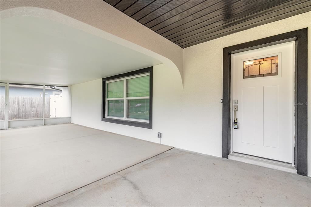 A covered concrete porch features a white front door and a window with dark trim — 2509 MILTON AVENUE, NEW SMYRNA BEACH, FL