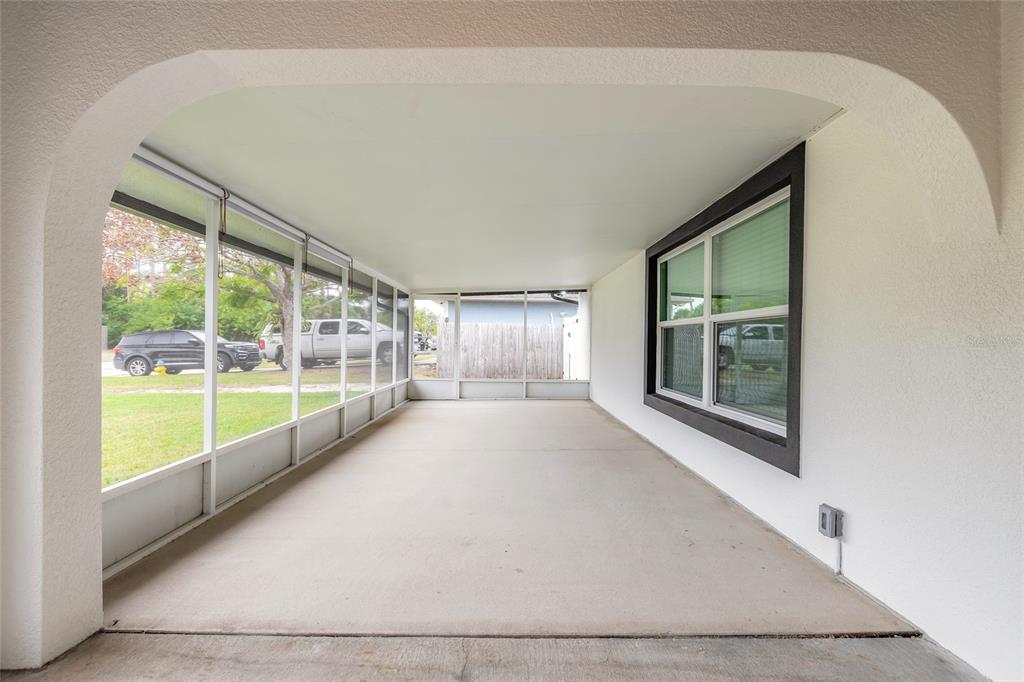 A screened-in porch with a concrete floor and a large window on the right wall — 2509 MILTON AVENUE, NEW SMYRNA BEACH, FL
