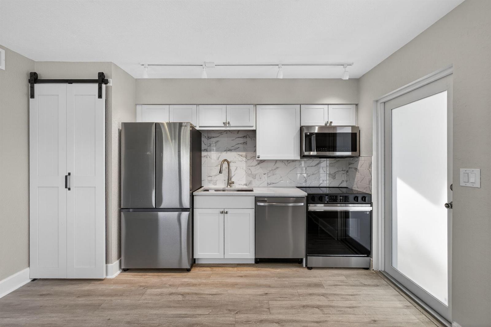 A kitchen features stainless steel appliances, white cabinets, a marble-patterned backsplash, and wood-look flooring — 624 Southwind Circle # 2, North Palm Beach FL 33408, NORTH PALM BEACH, FL