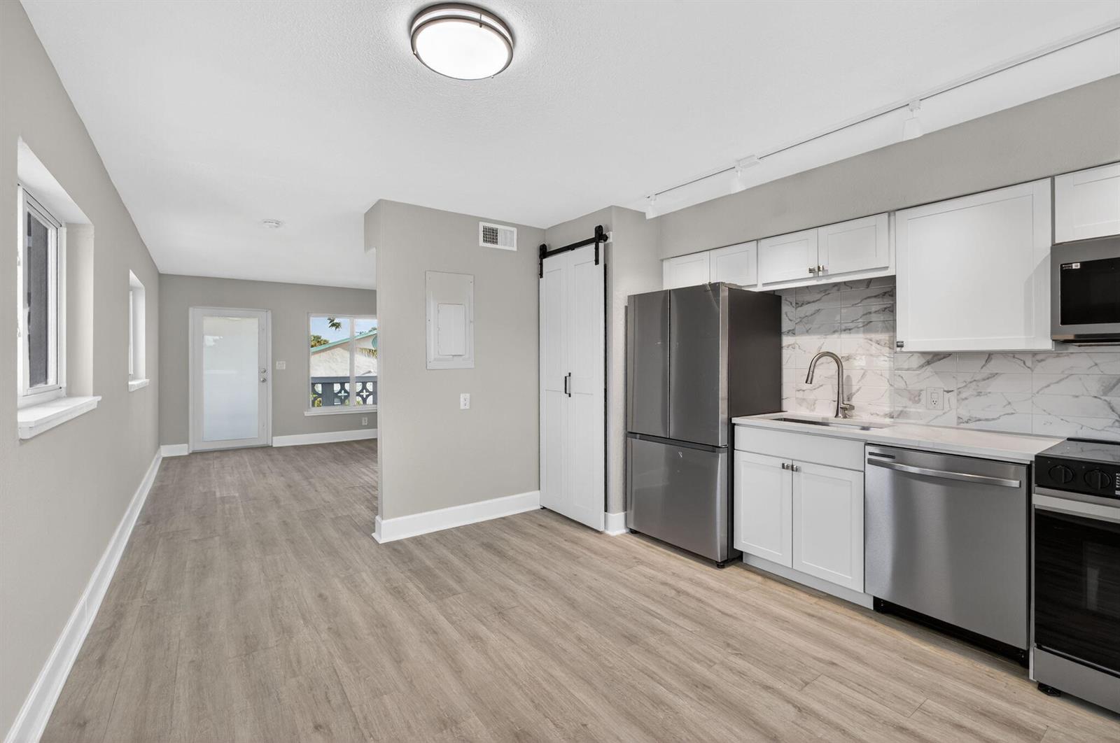 A kitchen with stainless steel appliances, white cabinets, and marble-look backsplash opens to a living area — 624 Southwind Circle # 2, North Palm Beach FL 33408, NORTH PALM BEACH, FL