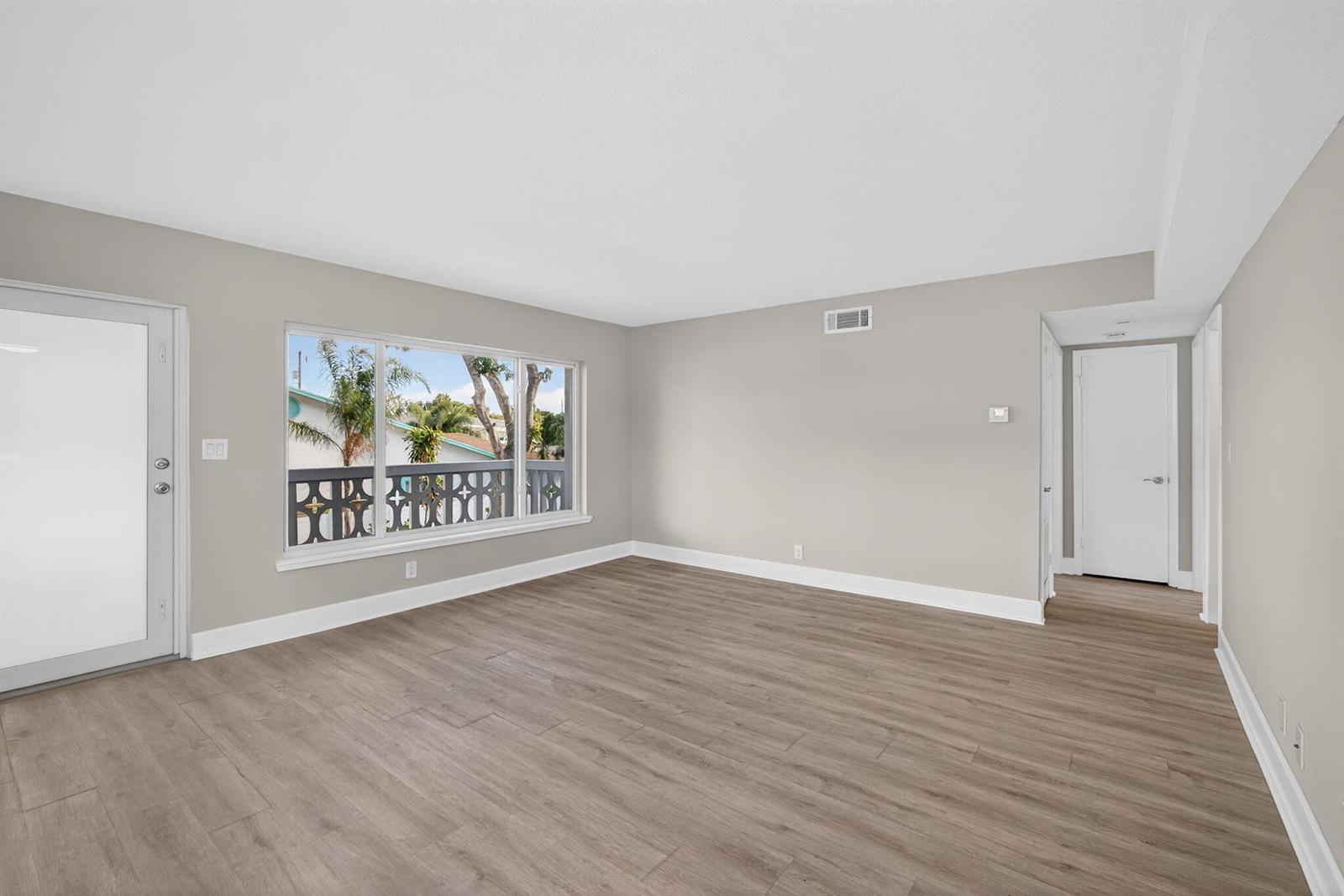 An empty room with light gray walls, wood-look flooring, a large window, and a door — 624 Southwind Circle # 2, North Palm Beach FL 33408, NORTH PALM BEACH, FL