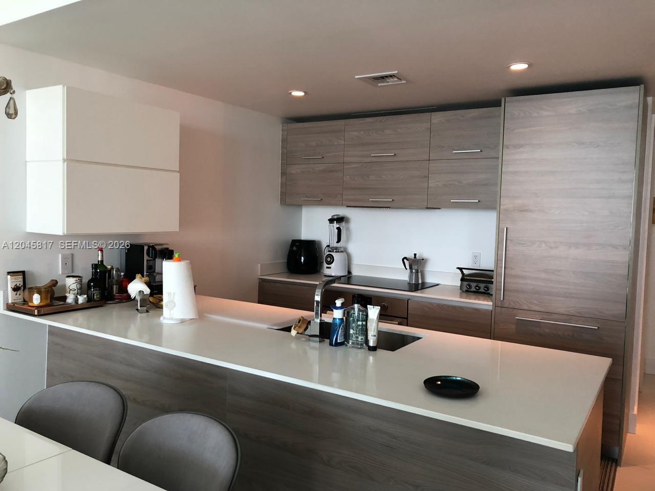 A modern kitchen features a white island countertop, wood-grain cabinetry, and stainless steel appliances — 1300 S Miami Ave # 3703, Miami FL 33130, MIAMI, FL
