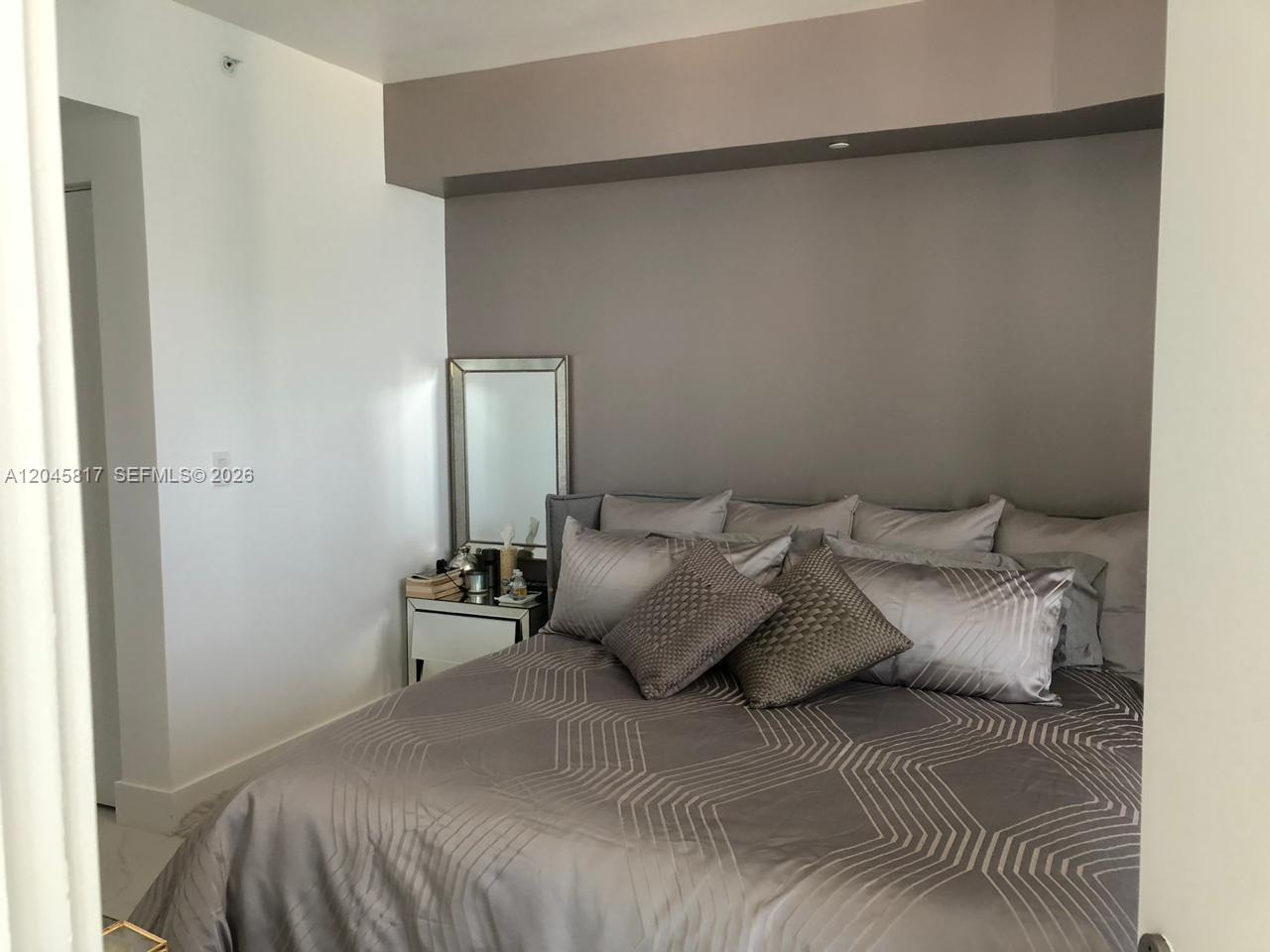 A bedroom features a gray bed with patterned bedding, a mirrored nightstand, and a gray accent wall — 1300 S Miami Ave # 3703, Miami FL 33130, MIAMI, FL