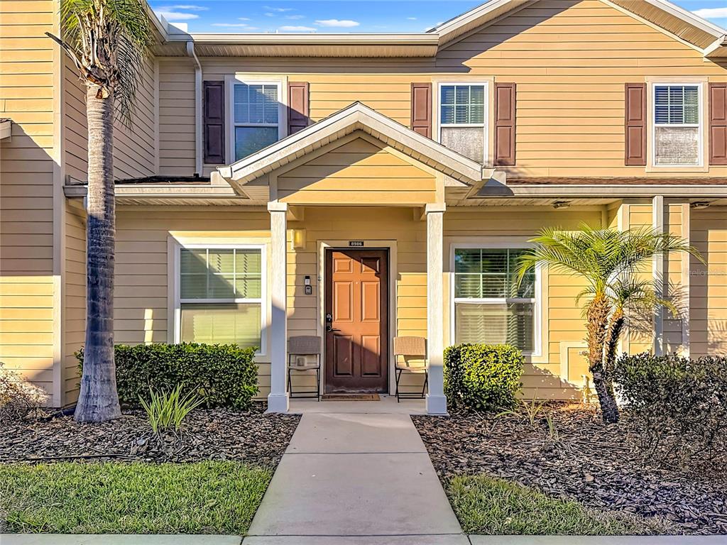 The exterior of a two-story tan townhouse features a covered entryway and a concrete walkway — 8986 SHINE DRIVE, KISSIMMEE, FL