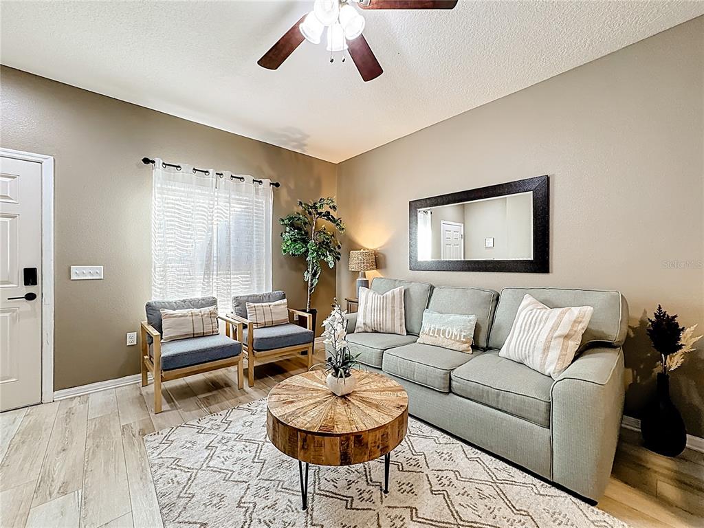 A living room features a gray sofa, two armchairs, a round wooden table, and a mirror — 8986 SHINE DRIVE, KISSIMMEE, FL
