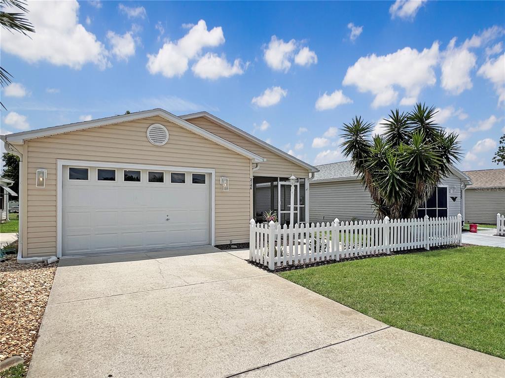 A single-story house with beige siding, a white garage door, and a white picket fence — 2146 ESTEVEZ DRIVE, THE VILLAGES, FL