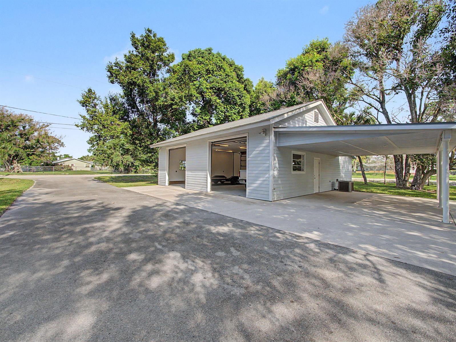 A detached garage with two open bays and an attached carport sits on a driveway — 5625 SE Ault Avenue, Stuart FL 34997, STUART, FL