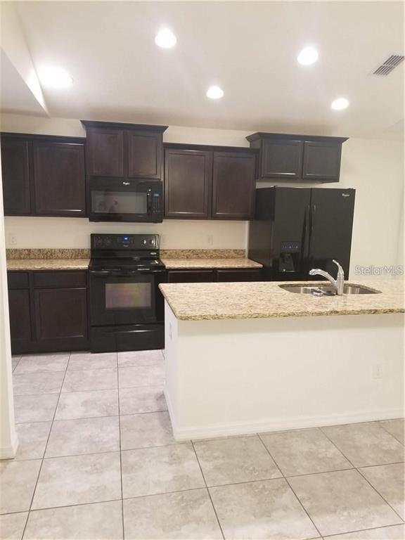 A kitchen features dark wood cabinets, granite countertops, black appliances, and light tile flooring — 1906 PONTOON PLACE, KISSIMMEE, FL