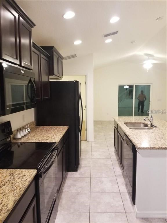 A kitchen features dark cabinets, granite countertops, stainless steel appliances, and light tile flooring — 1906 PONTOON PLACE, KISSIMMEE, FL