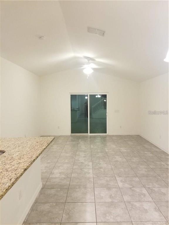 An open-concept room features light-colored tile flooring, a vaulted ceiling, and a sliding glass door — 1906 PONTOON PLACE, KISSIMMEE, FL