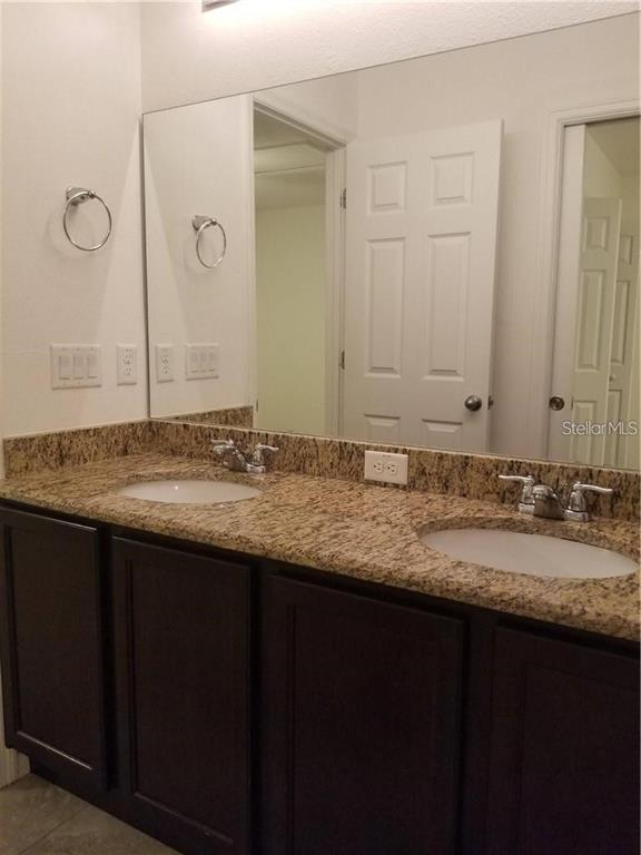 A bathroom vanity with a granite countertop, dual sinks, and a large wall mirror — 1906 PONTOON PLACE, KISSIMMEE, FL
