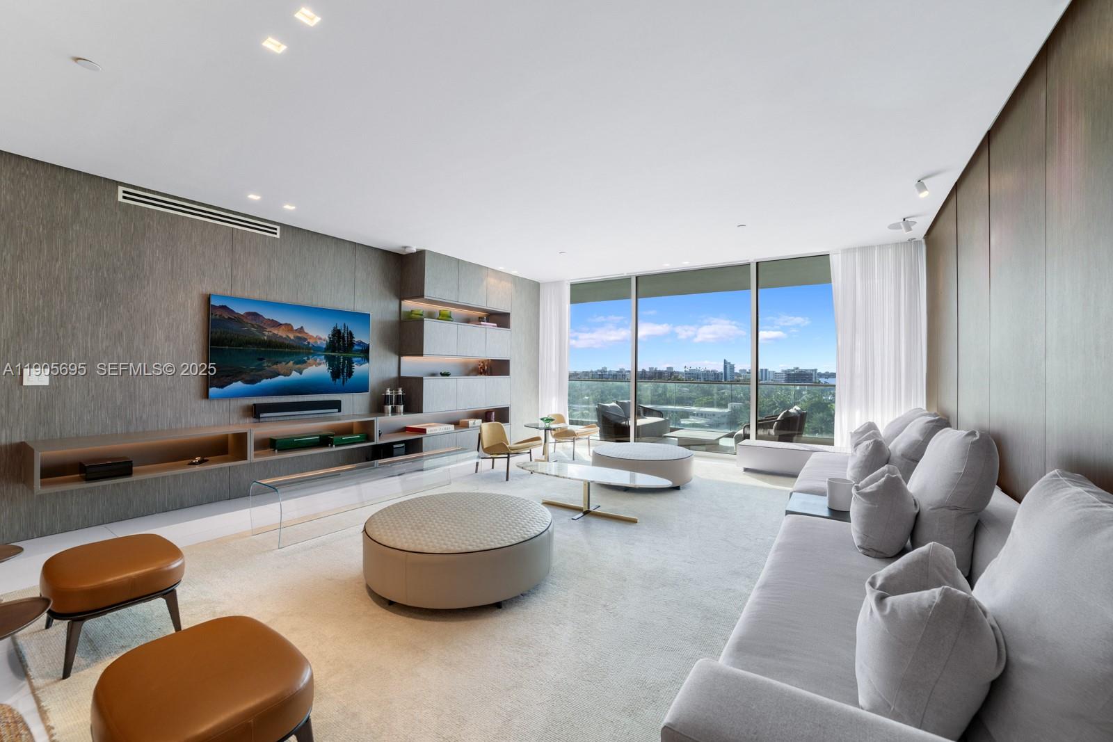 A modern living room features a large television, built-in shelving, and floor-to-ceiling windows with views — 10201 Collins Ave # 807, Bal Harbour FL 33154, BAL HARBOUR, FL