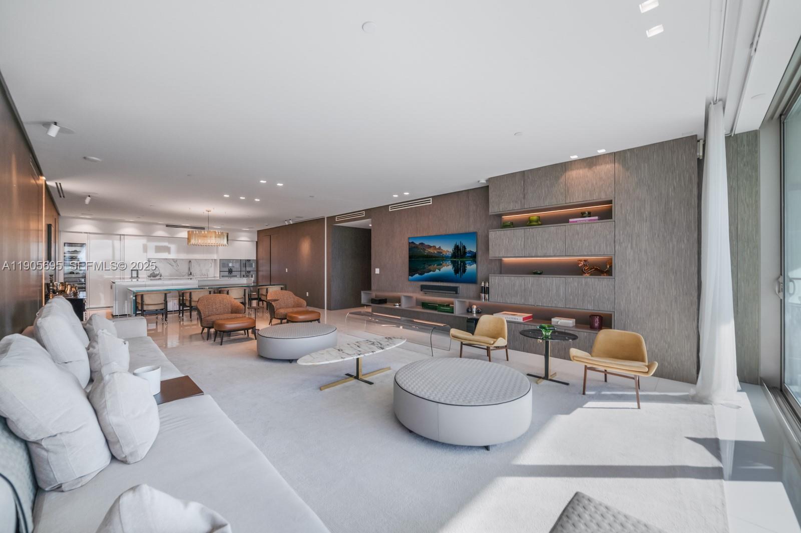 A modern open-concept living room features a large sofa, circular ottomans, and a media wall — 10201 Collins Ave # 807, Bal Harbour FL 33154, BAL HARBOUR, FL