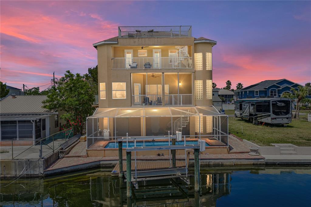 A three-story waterfront house with a screened pool, boat lift, and rooftop deck at sunset — 4178 DES PREZ COURT, HERNANDO BEACH, FL
