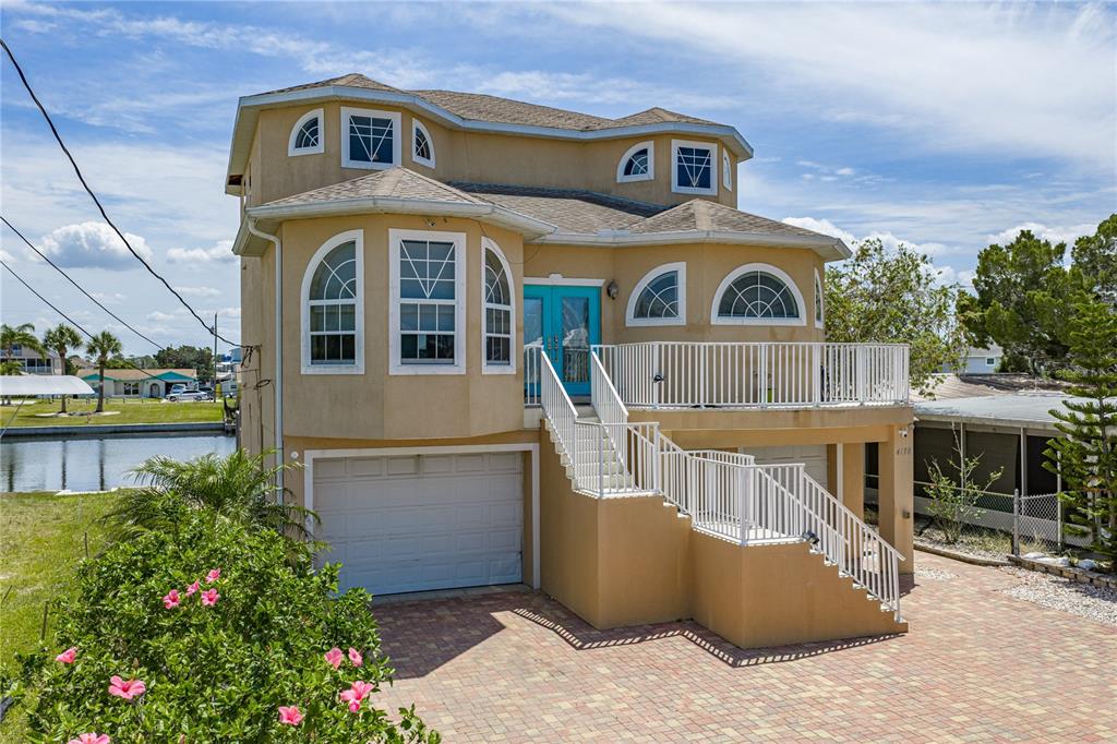An elevated tan house with a garage, a front staircase, and a balcony overlooking water — 4178 DES PREZ COURT, HERNANDO BEACH, FL