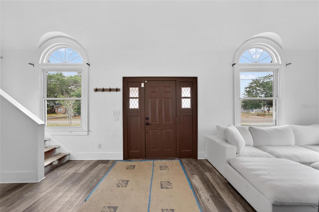 A living room features white walls, wood-look flooring, arched windows, and a dark brown front door — 1900 16TH STREET S, ST PETERSBURG, FL