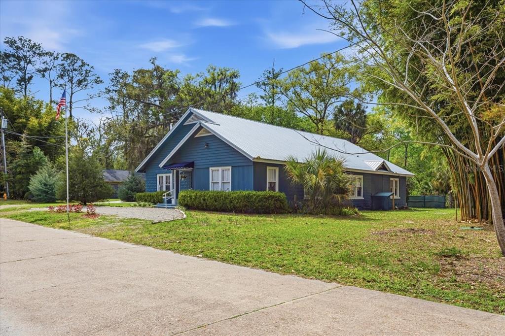A blue, single-story house with a metal roof sits on a grassy lot with trees — 18708 NW 242ND STREET, HIGH SPRINGS, FL