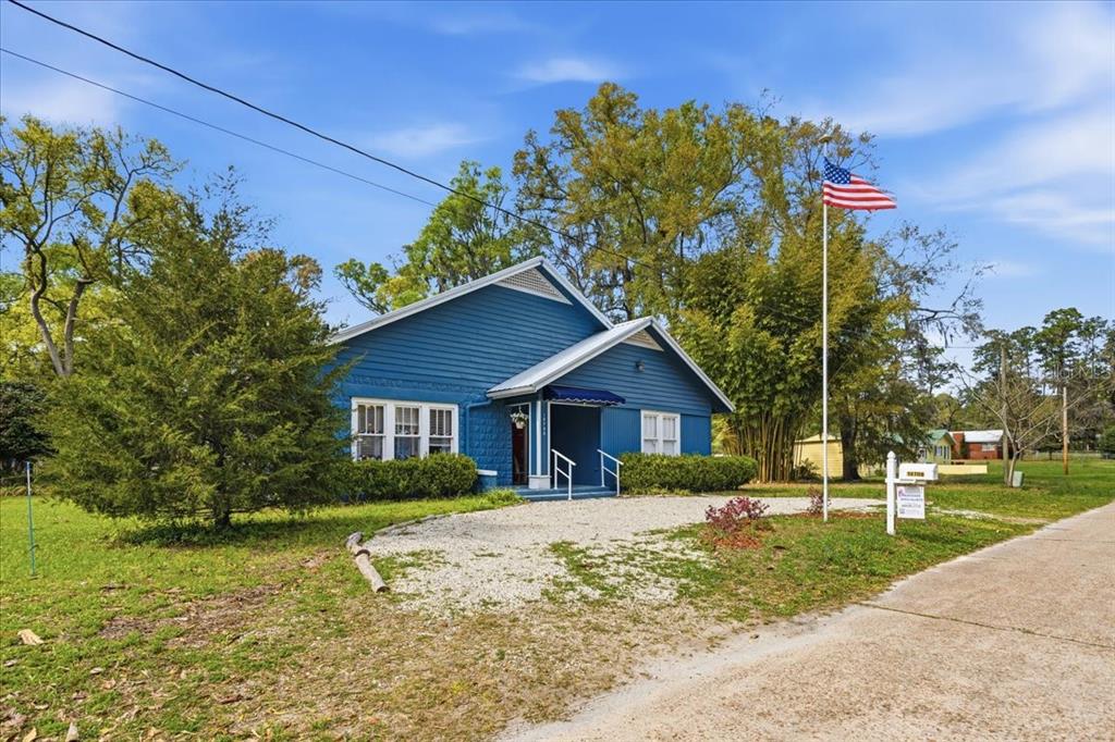 A blue, single-story house with a gravel driveway and an American flag on a pole — 18708 NW 242ND STREET, HIGH SPRINGS, FL