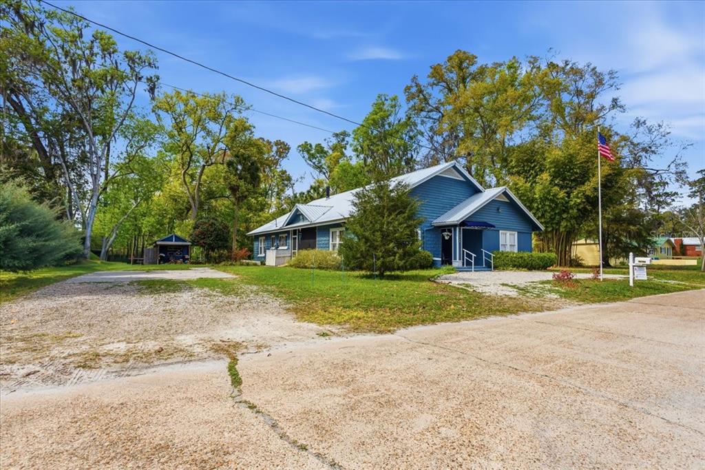 A blue house with a metal roof sits on a gravel lot with trees — 18708 NW 242ND STREET, HIGH SPRINGS, FL