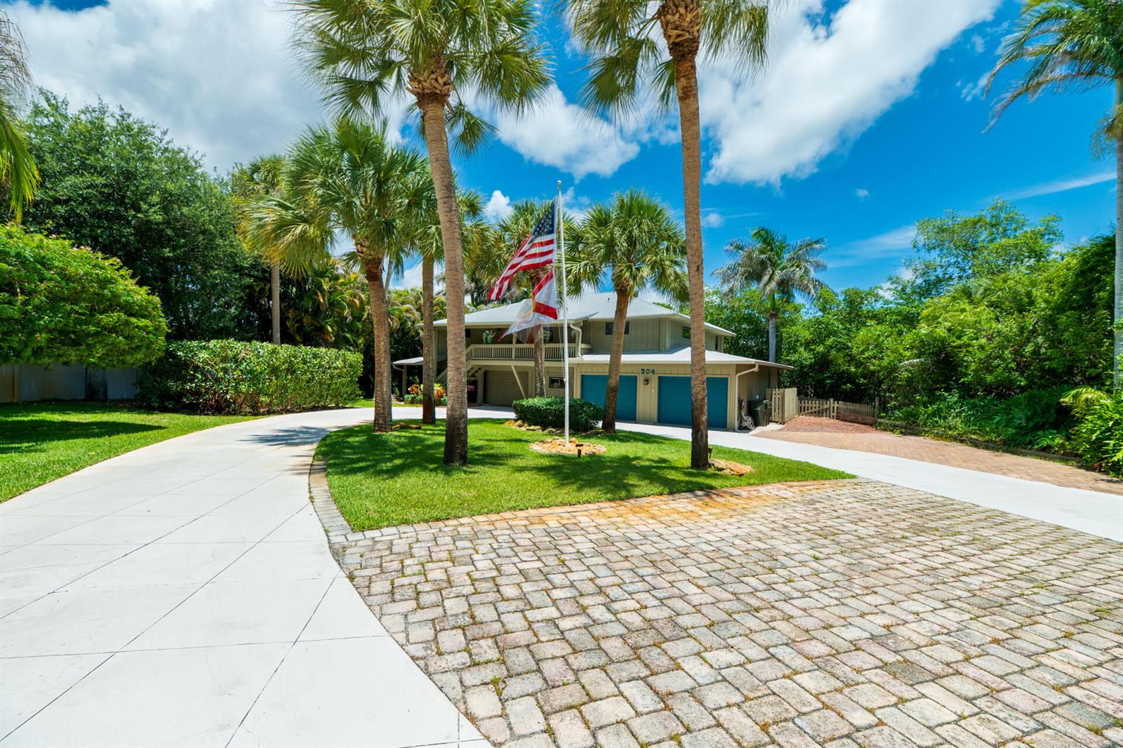 A two-story house with a paved driveway, palm trees, and an American flag — 304 SW Indian Groves Drive, Stuart FL 34994, STUART, FL