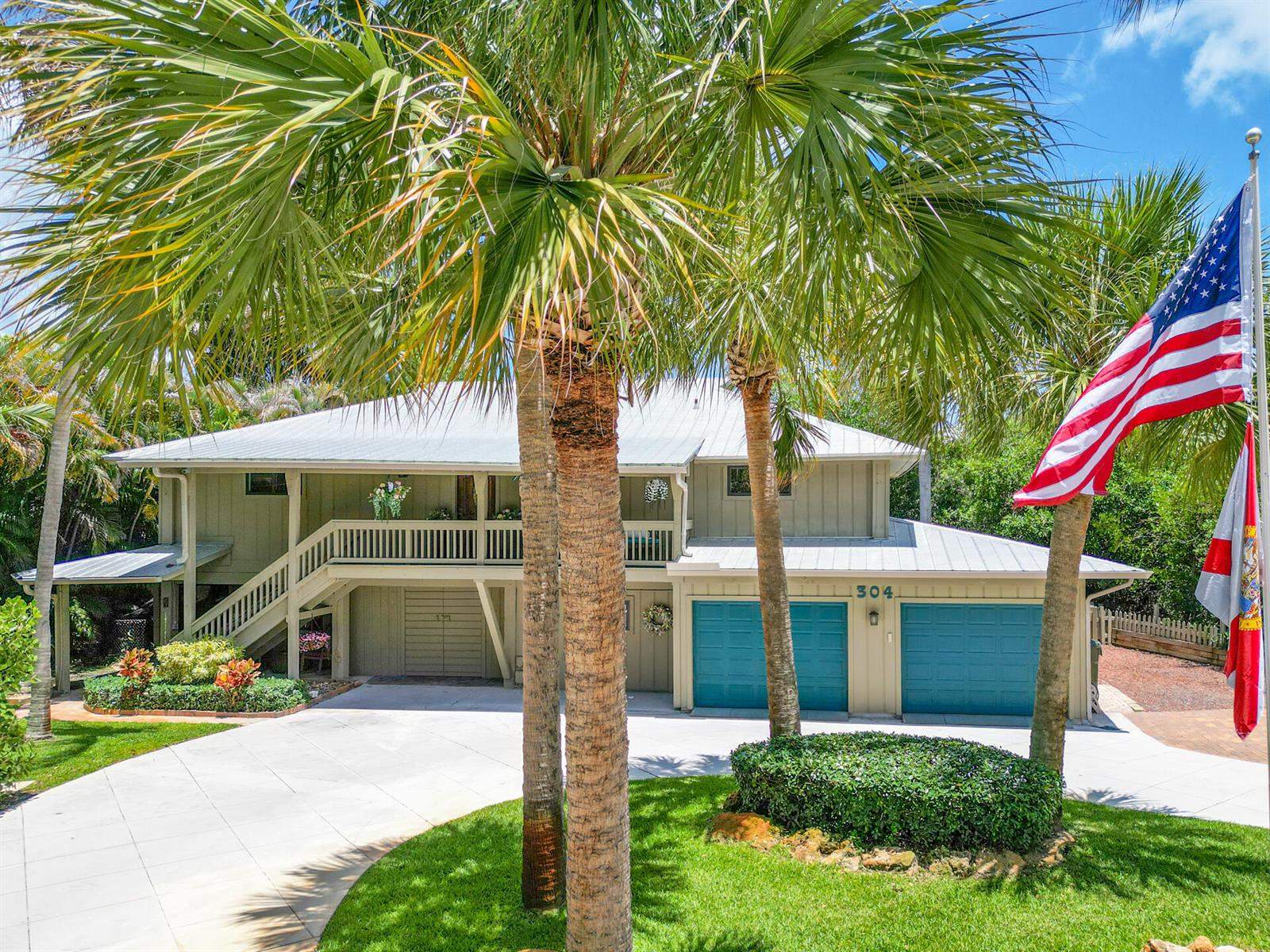 A two-story house with a metal roof, blue garage doors, and palm trees in front — 304 SW Indian Groves Drive, Stuart FL 34994, STUART, FL