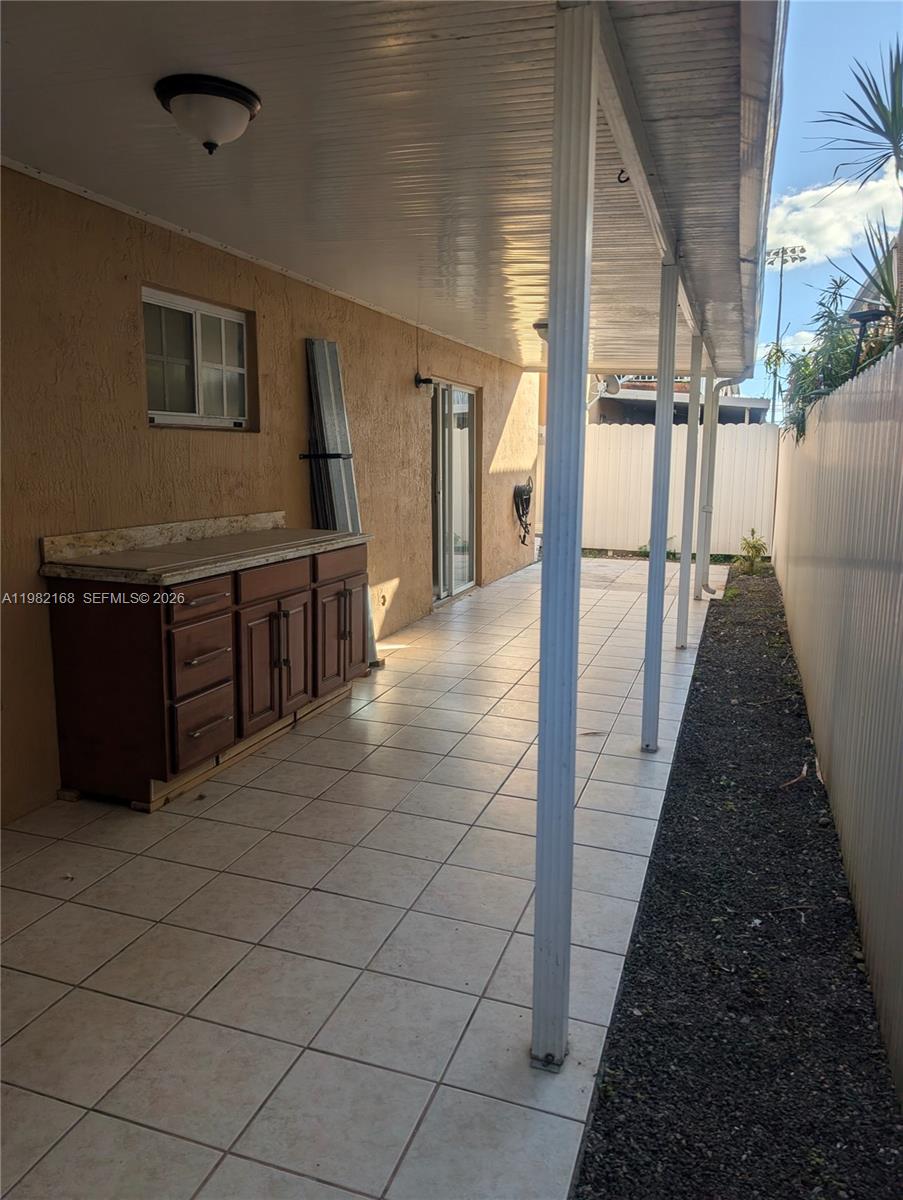 A covered outdoor patio features tiled flooring, a wooden cabinet, and a white privacy fence — 2485 W 76th St # 109, Hialeah FL 33016, HIALEAH, FL