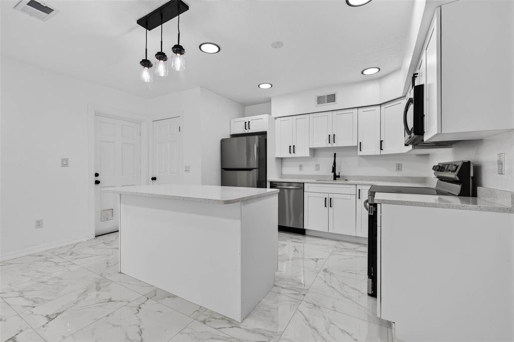 A modern kitchen features white cabinets, stainless steel appliances, a center island, and marble-look flooring — 2801 45TH STREET S, ST PETERSBURG, FL