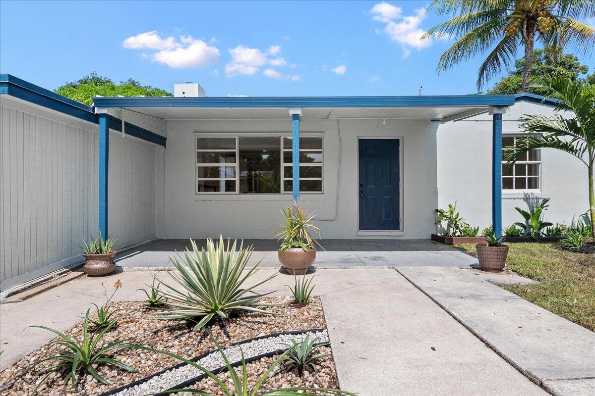 The exterior of a single-story house features a covered patio, blue trim, and desert landscaping — 1306 S C Terrace, FL 33460, FL
