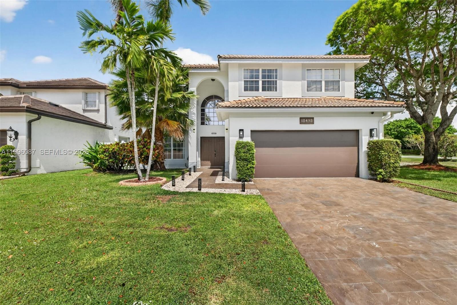 A two-story house features a brown garage door, a tiled roof, and palm trees — 18498 E Covington Trce, Boca Raton FL 33498, BOCA RATON, FL